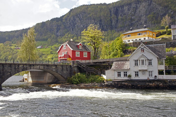 Fototapeta na wymiar White and red scandinavian houses and the bridge over the foamy wild water of the fjord on the Norwegian countryside