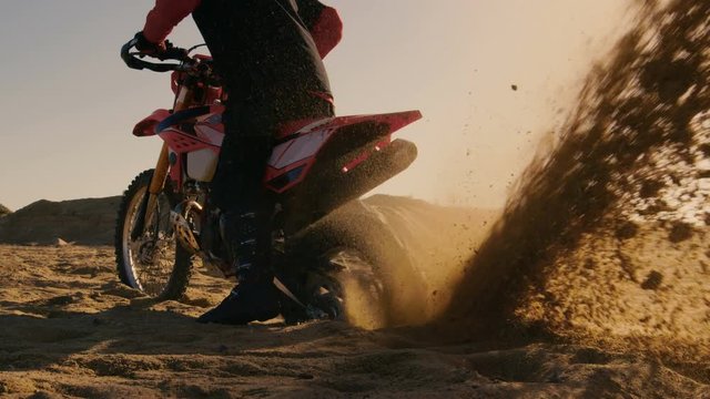 Back View Footage of the Professional Rider on the FMX Dirt Bike Twisting Full Throttle Handle and Digging into the Sand with His Back Wheel