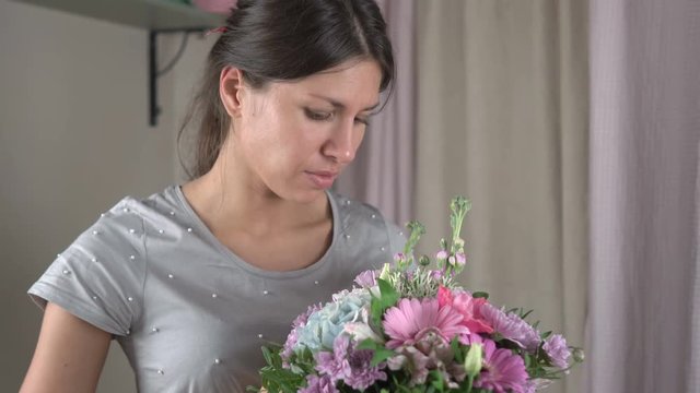 Female florist finishes making a bouquet of flowers in a hat box and happily looks at him close-up 4k.