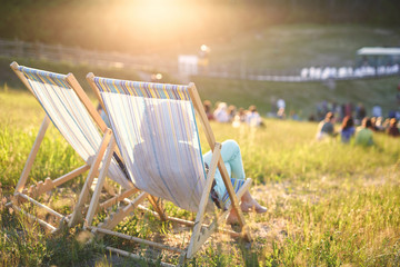 back view of young woman in sun glasses sitting in a lounge chair at a picnic on a bright sunny day