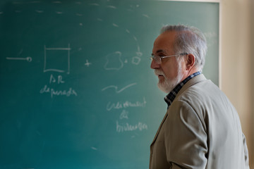 Mature professor in the classroom with green blackboard