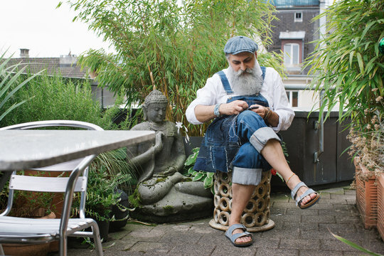 Environmental Portrait of Cool Senior Man With Grey Beard Stitching on Rooftop Terrace