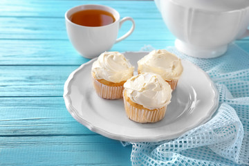 Plate with tasty vanilla cupcakes and cup of tea on table