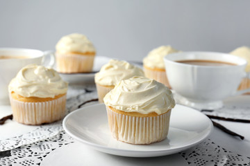 Tasty vanilla cupcakes and cups on table