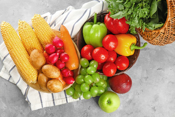 Fresh fruits and vegetables in wicker bowls on grey background