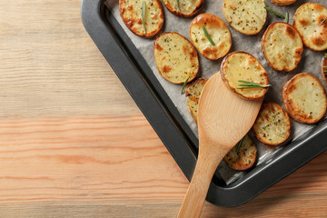 Baking tray with spatula and delicious baked potatoes on wooden background
