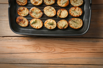 Grill pan with delicious baked potato slices on table