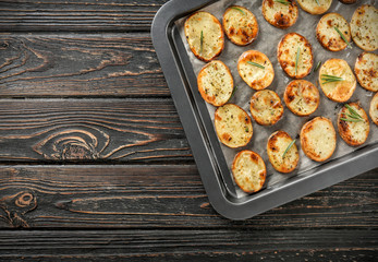 Baking tray with delicious baked potatoes on wooden background
