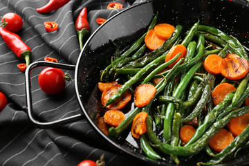 Delicious green beans and carrot slices in frying pan on black fabric