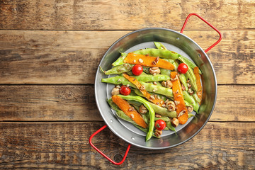 Frying pan with delicious green beans, carrot and cherry tomatoes on wooden background
