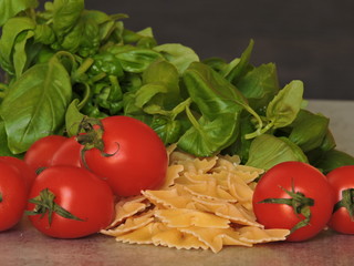 Basil, pasta bows, cherry tomatoes, basil, olives, salt. Recipe. Macro. Copy space.