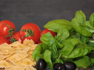 Pasta bows, cherry tomatoes, basil, olives, salt. Recipe. Macro. Copy space.