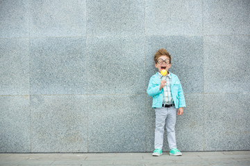 Obraz na płótnie Canvas Fashion kid with lollipop near gray wall