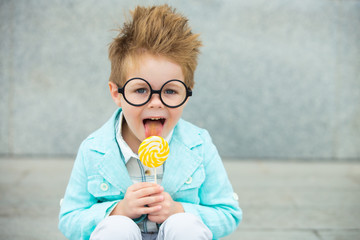 Fashion kid with lollipop near gray wall