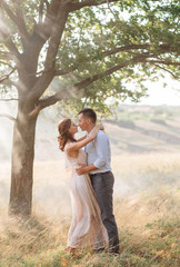 Fototapeta premium Beautiful love story in the fog with the rays of the sun.. Couple in love in the evening haze. Creative colors