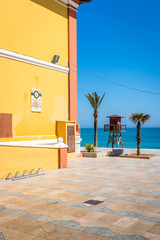A typical yellow building by the mediterranean sea with palm trees and a lifeguard stand