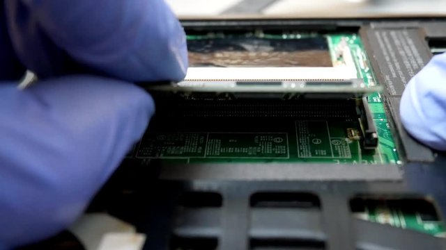 Hands in blue gloves takes out dimm ram memory in notebook in the service center for repair and upgrade of computers or laptop