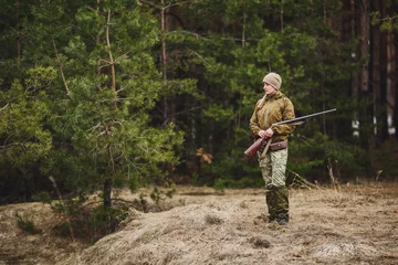 Cercles muraux Chasser Female hunter in camouflage clothes ready to hunt, holding gun and walking in forest.