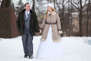 Happy and smiling wedding couple walking together in winter park, holding hands