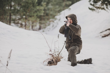 male hunter ready to hunt, holding gun and sitting in forest.
