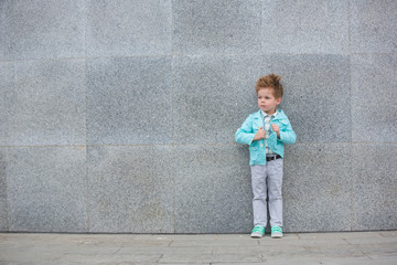 Fototapeta na wymiar Fashion kid posing near gray wall