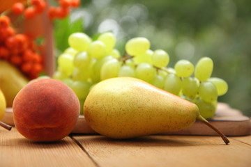 Pears, peach, green grapes, rowan berries in a wooden box on a wooden table in the woods at the time of harvesting