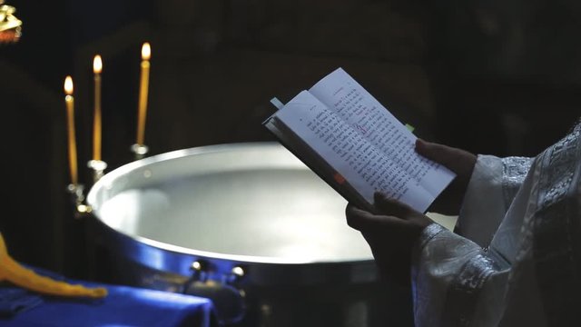 before the ritual baptism of water, the priest reads old prayer book. Clergyman performs a ritual, reads and is baptized, next to the chaplain is a bowl of consecrated water