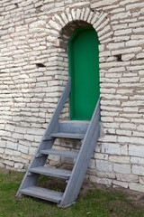 Green metal door in brick wall with wooden stairs from land