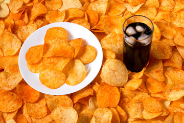 Golden Chips potato texture. Chips on a white plate standing on a large pile of chips with glass of...