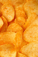 Fototapeta premium background of crispy golden chips with ribbed texture, seasoned, with sunlight. Frame for wallpapers, background, and texture. Vertical