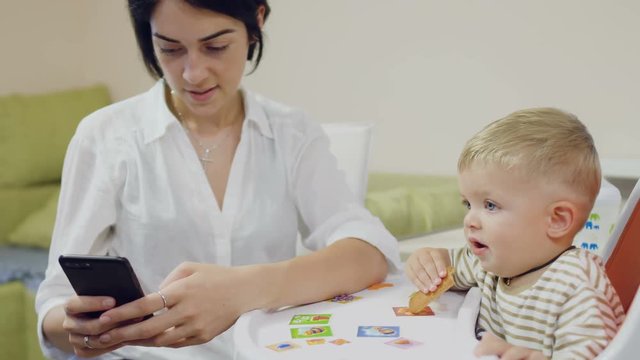 Mother uses phone during little son eating biscuit