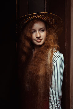 Beautiful ginger model with freckles in straw hat posing in old passage