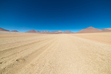 Fototapeta na wymiar Dirt road at high altitude with sandy desert and barren volcano range on the Andean highlands. Road trip to the famous Uyuni Salt Flat, among the most important travel destination in Bolivia.