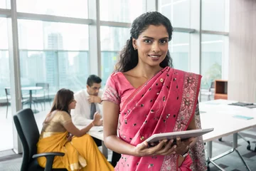 Fotobehang Confident Indian business woman looking at camera while holding a tablet in a modern meeting room © Kzenon