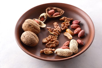 Walnuts and peanuts on a brown clay plate on a white background