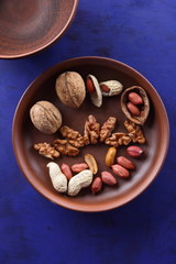 Walnuts and peanuts on a brown clay plate on a blue background