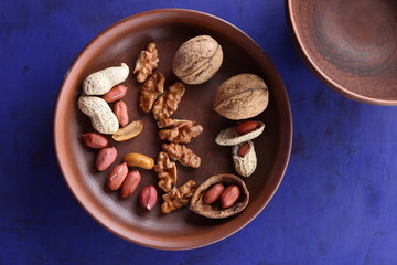 Fototapeta na wymiar Walnuts and peanuts on a brown clay plate on a blue background