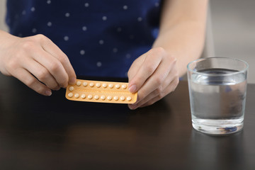 Woman with birth control pills and glass of water at table