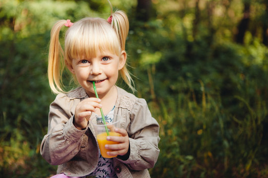 Cute little girl drink orange juice outdoors