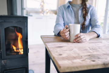 Woman with cup of coffee sitting by the fireplace and wooden table