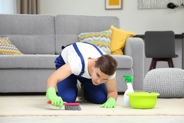 Man cleaning carpet with brush in living room