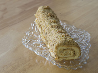 whole caramel swiss roll with walnuts on decorative glass platter with on wooden table background