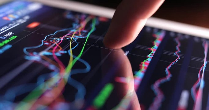 Finger touch on tablet computer screen with stock market graph