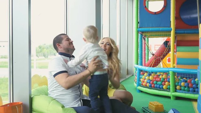 Father throws up little cute two-year-old son in the hands indoor of children's entertainment center. Mother looks after the child