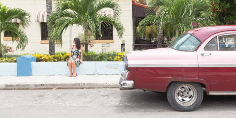 Fashionable girl with a classical old american car in Cuba
