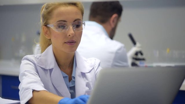 Smart female scientist in safety glasses typing on computer