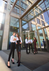 two young pretty girls or business women in office style clothes with a tablet in their hands discuss the plan against the backdrop of colleagues or employees of the company