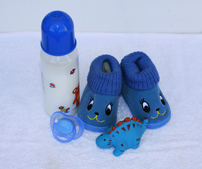 Set for newborn boy with baby milk, toy, pacifier, anti cute funny blue shoes on white background.