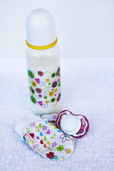 Set for newborn girl with baby milk,  pacifier, anti scratch hand guard mittens on white background.