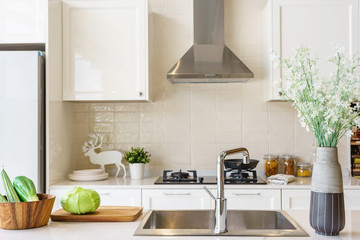 Counter top made in ceramic seen closely with fruits and vegetable on a brown color clay dish next to the modern silver faucet attached to the sink, the silver refrigerator .
